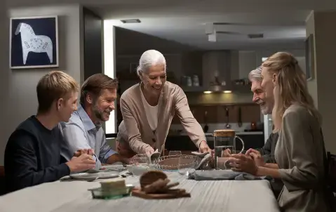 משפחה רב-דורית יושבת סביב שולחן אוכל בזמן שאישה מבוגרת מגישה מאפה חם